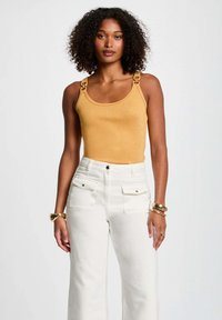 Yellow metallic tank top with square hardware on straps, paired with white high-waisted wide-leg pants featuring front pockets.