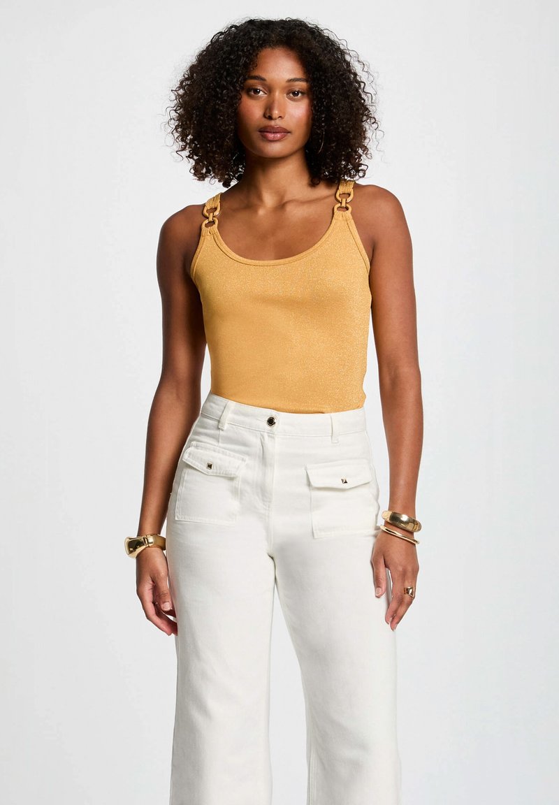 Yellow metallic tank top with square hardware on straps, paired with white high-waisted wide-leg pants featuring front pockets.