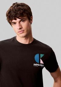 Camiseta de algodón negra con el logo colorido de Calvin Klein en el pecho izquierdo, con cuello redondeado y mangas cortas.