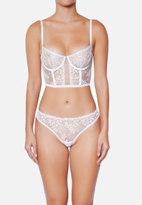 Ensemble de lingerie en dentelle blanche comprenant un bralette semi-transparent avec broderies florales et un shorty taille haute assorti avec des bords festonnés.