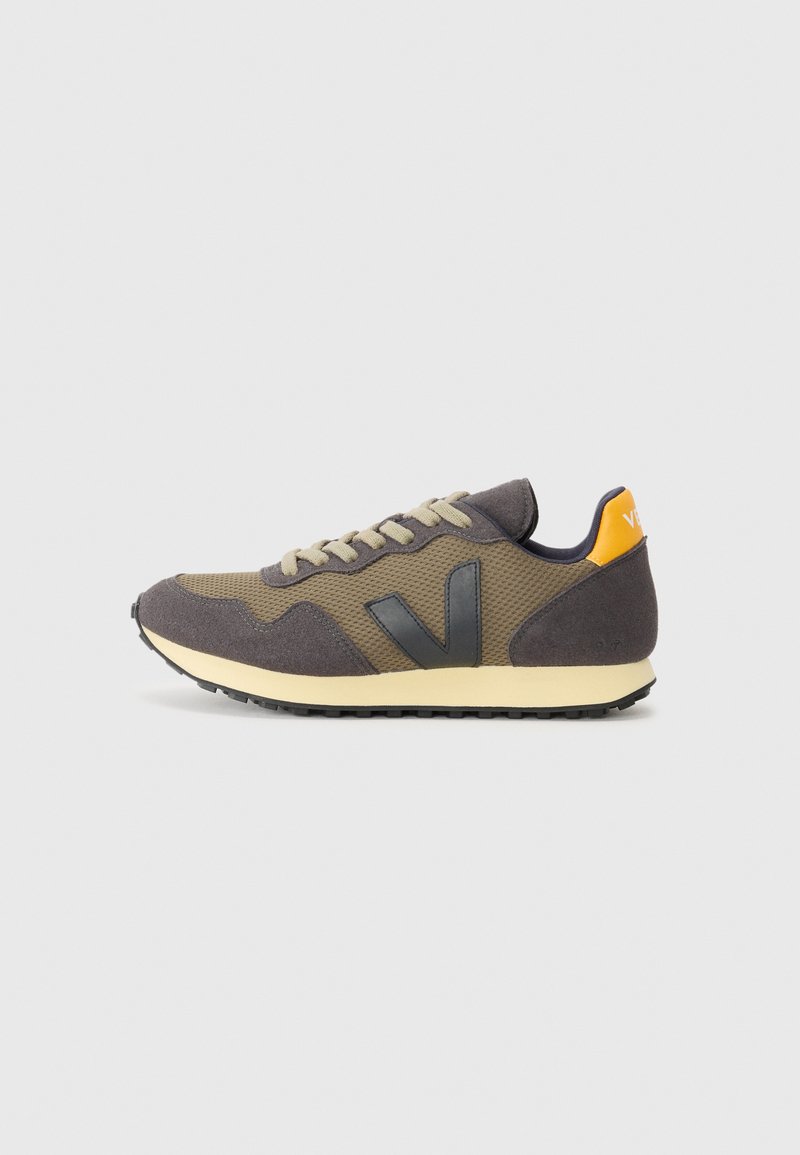 Tenisi cu un brâu din plasă și suede în nuanțe de gri și khaki, având un logo negru, o talpă intermediară bej și un accent portocaliu pe călcâi.