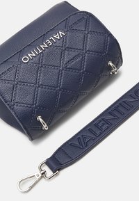 Námorně modrá prošívaná taška s stříbrným logem "VALENTINO" na přední straně, vybavená odnímatelným popruhem se stejným brandingem.