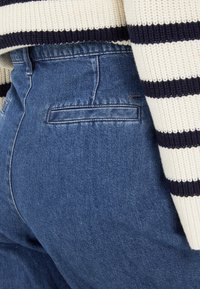 Donkerblauwe denim jeans met een gladde textuur en een detail op de achterzak, gecombineerd met een crèmekleurige en marineblauwe gestreepte gebreide trui.