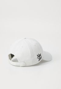 Cappello bianco in cotone con visiera curva, dotato di ricamo con il testo "New York" in nero su un lato e di una fascia regolabile sul retro.