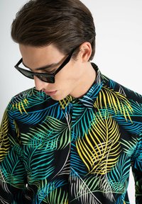 Camisa negra de botones con un vibrante patrón de hojas de palma en verde, amarillo y azul. El tejido parece ligero y suave.