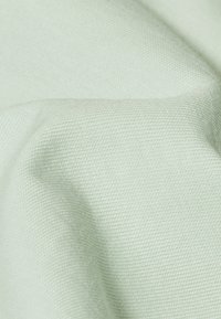 Jasnozielony materiał o gładkiej, teksturowanej powierzchni. Tkanina jest o drobnym splocie, który ukazuje subtelny wzór, podkreślający jej jakość dotykową.