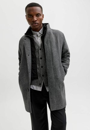 Grijze wollen blend overjas met hoge kraag, gelaagd over een grijze vest en gestreefd shirt. Bevat knopen en heeft een soepele textuur.