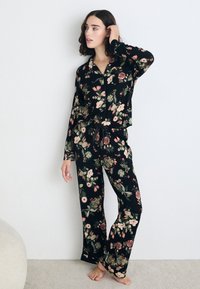Zwart pyjama set met bloemenpatroon, voorzien van lange mouwen en broek, gemaakt van zacht materiaal met een strikdetail in de taille.