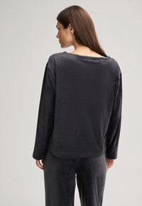 Zwart velours loungepak bestaande uit een losse lange mouwen top met een brede halslijn en comfortabele broeken met een elastische tailleband.