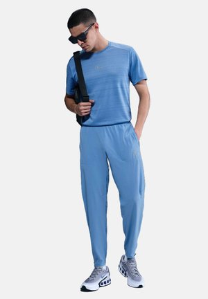 Lys blå sportsoutfit bestående af en kortærmet skjorte og tætsiddende bukser, lavet af åndbart materiale. Udsmykket med et logo.