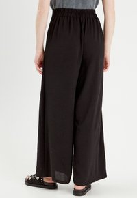 Pantalons larges noirs en tissu texturé. Dotés d'une taille élastique et d'une coupe ample. Associés à des sandales noires.