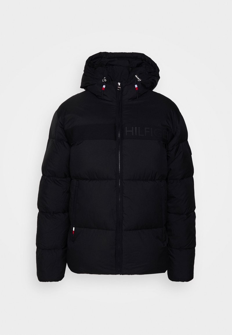 Doudoune noire avec capuche, fermeture éclair devant et petits détails de drapeau rouge, blanc et bleu sur les manches et les cordons de la capuche.