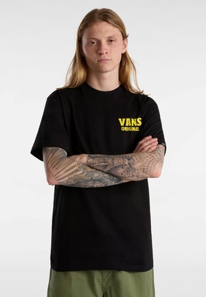 Camiseta de algodón negra con un logo amarillo de "VANS ORIGINAL" en el pecho. La camiseta tiene mangas cortas y un diseño de cuello redondo.