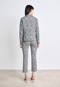 Angepasstes Anzugset in einem geometrischen Schwarz-Weiß-Muster. Die Jacke hat einen Kragen und einen strukturierten Stoff; die Hose ist tailliert und ausgestellt.