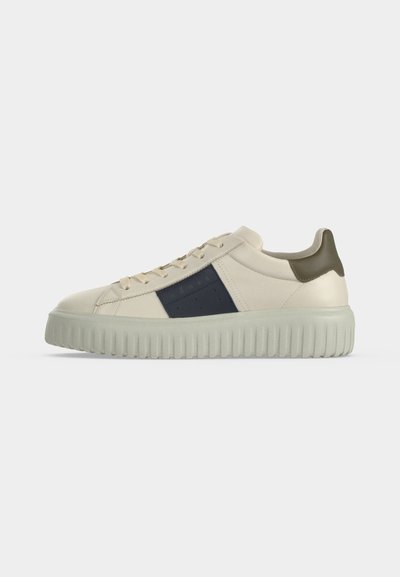 Baskets basses crème avec semelle épaisse gris clair, bande bleu foncé sur le côté et patch talon vert olive, présentées sur fond uni.