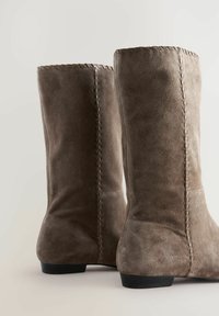 Brown suede ankle boots with stitched detailing, flat black heels, and a textured surface. The design features a rounded toe and mid-calf height.