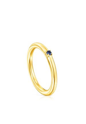 Gold ring with a smooth, rounded design, featuring a small blue gemstone set in a prong. Reflective and polished surface finish.