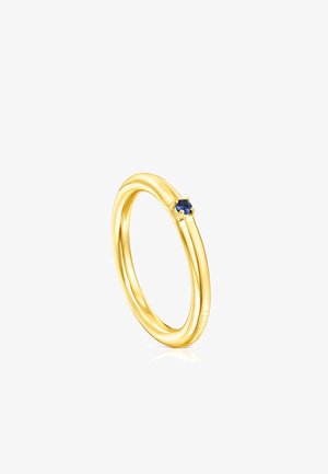 Anillo de oro con un diseño liso y redondeado, que presenta una pequeña gema azul engastada en un bisel. Acabado de superficie reflectante y pulida.