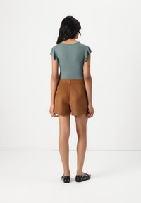 Teal ribbed bodysuit with ruffled sleeves, paired with brown suede shorts. Model wears black flat shoes with circular accents.