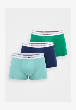 Trzy pary męskich kąpielówek: jedna w odcieniu teal, jedna w zielonym, a jedna w granatowym. Każda z nich ma białą gumkę w pasie z czerwonym i granatowym brandingiem.