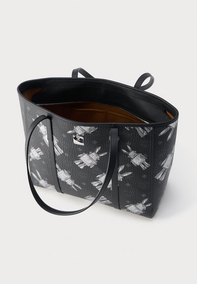 Μαύρη τσάντα tote από δέρμα με υφή, μοτίβο λευκού ρομποτικού λαγού, διπλές λαβές και ανοιχτή κορυφή που αποκαλύπτει καφέ εσωτερική επένδυση.