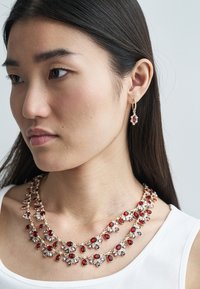 Rode en paarse edelstenen ketting met gouden accenten, gelaagd ontwerp met druppelvormen. Bijpassende oorbellen met een vergelijkbare steenindeling.