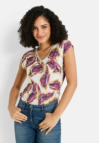 Blusa de flores de manga corta y escote en V con base blanca, que presenta patrones de hojas en púrpura, amarillo y rosa. Fabricada en una tela ligera y texturizada.