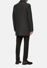 Grau melierter Wollmischmantel mit taillierter Passform, Reverskragen und strukturiertem Finish, kombiniert mit schwarzen Hosen und Schuhen.