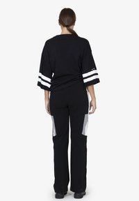 Zwart oversized shirt met witte strepen op de mouwen, gecombineerd met zwarte broek met grijze zijpanelen en een losse pasvorm.