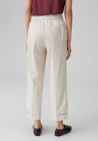 Lichtbeige broeken met een relaxte pasvorm, elastische tailleband, afgeknipte zomen en zakken, gedragen met donkerbruine instappers.