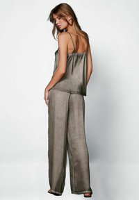 Satinová camisole v tlumené olivové barvě s nastavitelnými ramínky, doplněná širokými kalhotami s volným střihem ve stejném materiálu a barvě.