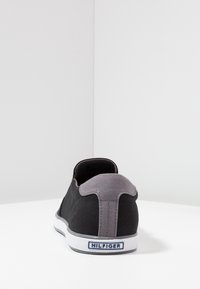 Czarne canvasowe buty wsuwane z szarym akcentem na pięcie i białą gumową podeszwą. Posiadają niebieską metkę z napisem "HILFIGER" na tyle.