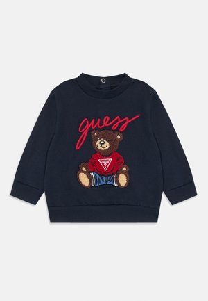 Navy sweatshirt featuring a textured bear graphic with a red shirt and blue shorts. Includes "guess" logo in red cursive on front.