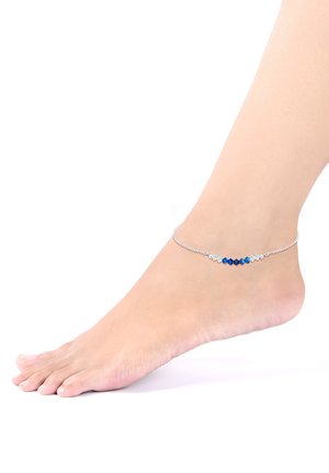 Silbernes Knöchelarmband mit blauen und klaren Perlen in verschiedenen Formen, das auf einem nackten Fuß vor einem weißen Hintergrund liegt.