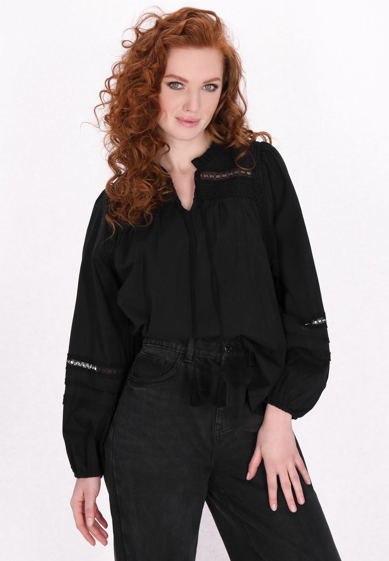 Zwarte blouse met lange, geraffineerde mouwen, uitgesneden kantaccenten en een V-halslijn. Gecombineerd met donker, high-waisted jeans.