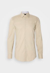 Chemise beige à manches longues boutonnée, col pointu et col intérieur blanc avec petits motifs noirs.