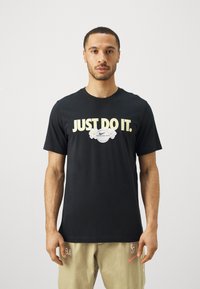 Svart bomullst-skjorte med teksten "JUST DO IT." i gul farge og et Nike-logo med blomsterdekorasjoner foran. Rund hals, kortermet.