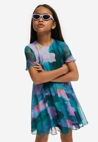 Korte mouwen, bloemenpatroon jurk in teal en paarse tinten met een uitlopende silhouet en geschulpte randen, gecombineerd met lichtpaarse zonnebril.