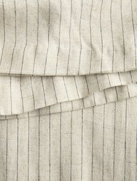 Tessuto beige con texture e sottili strisce verticali nere, che mostra un aspetto morbido e intrecciato con una leggera lucentezza. I bordi sono rifiniti con cura.