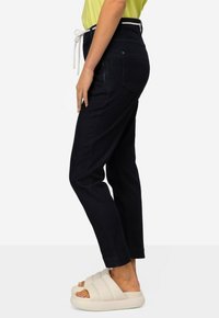 Pantaloni in denim blu scuro con una vestibilità comoda, dotati di vita con cordino e tasche laterali, abbinati a sandali scivolati di colore crema.