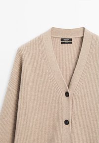 Cardigan en laine beige avec texture en maille côtelée, col en V et deux boutons noirs sur le devant.