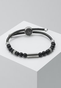 Bracciale nero caratterizzato da un design con perline, con pietre nere opache e accenti in argento, una chiusura a logo rotondo e una placca rettangolare "DIESEL".