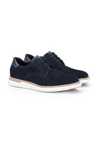 Chaussures en suede bleu marine avec un capuchon de talon en cuir lisse, cinq œillets et une semelle en caoutchouc blanche avec une bande d'accent marron clair.