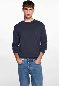 Mornarska nedrčna majica iz mešanice bombaža, z ribastimi manšeti in robom, v kombinaciji s svetlo modrimi kavbojkami.