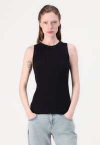 Svart ribbet ermeløs topp med rund hals, laget av teksturert stoff, sammen med lyseblå løse jeans.