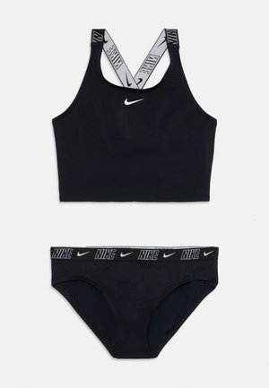Top desportivo preto com alças cruzadas apresentando o logótipo branco da Nike. Parte de baixo do biquíni preta combinando com uma faixa na cintura com a marca Nike em branco.