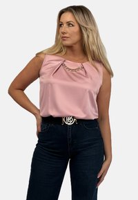 Różowa satynowa bluzka bez rękawów z przodem w plisę i złotym akcentem. Połączona z ciemnymi, wysokogatunkowymi dżinsami i paskiem z złotym okuciem.