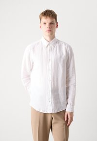 Hvit langermet skjorte med knapper i lett lin, med krage, subtil tekstur og en liten brodert logo på brystet.