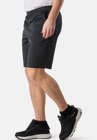 Grå sportshorts med ett elastiskt midjeband. Tyget har en melerad struktur. Bärs med svarta sneakers och ankelstrumpor.
