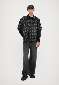 Black short-sleeve shirt with gray diamond pattern, layered over a black long-sleeve shirt. Paired with gray wide-leg jeans and black sneakers.